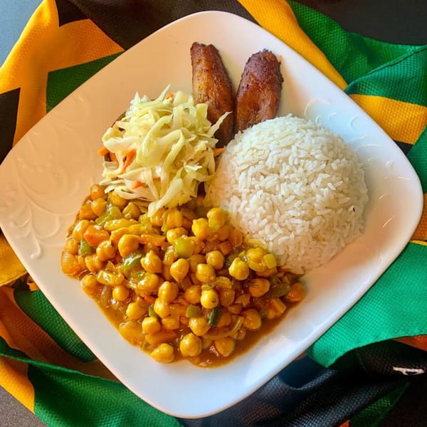 A Jamaican chickpea curry with white rice, coleslaw, and fried plantains on a white plate.
