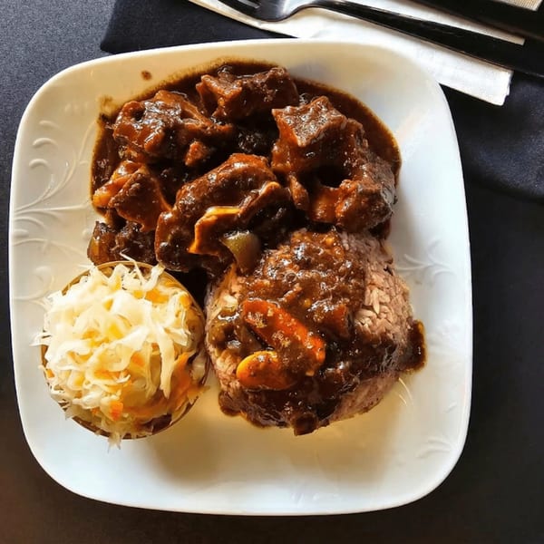 A plate of Jamaican oxtail stew with rice and peas, and a side of coleslaw.