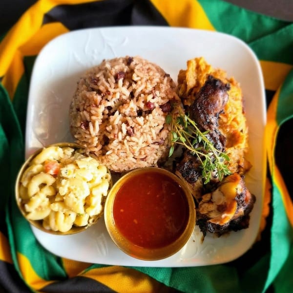 A Jamaican meal with rice and peas, jerk chicken, macaroni and cheese, and red sauce.
