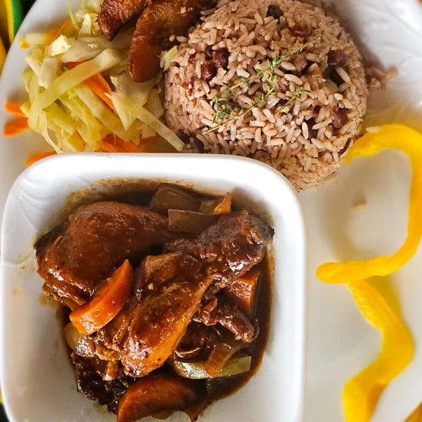 A plate of brown stew chicken, rice and peas, steamed cabbage, and plantains.