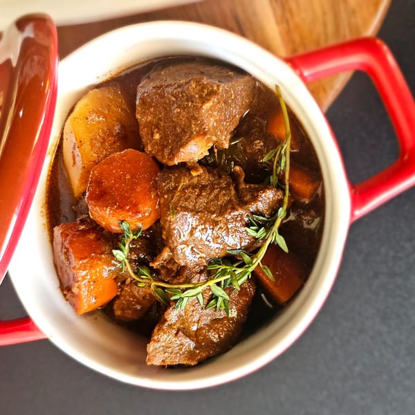 Hearty beef stew with carrots, potatoes, and fresh thyme in a red and white pot.